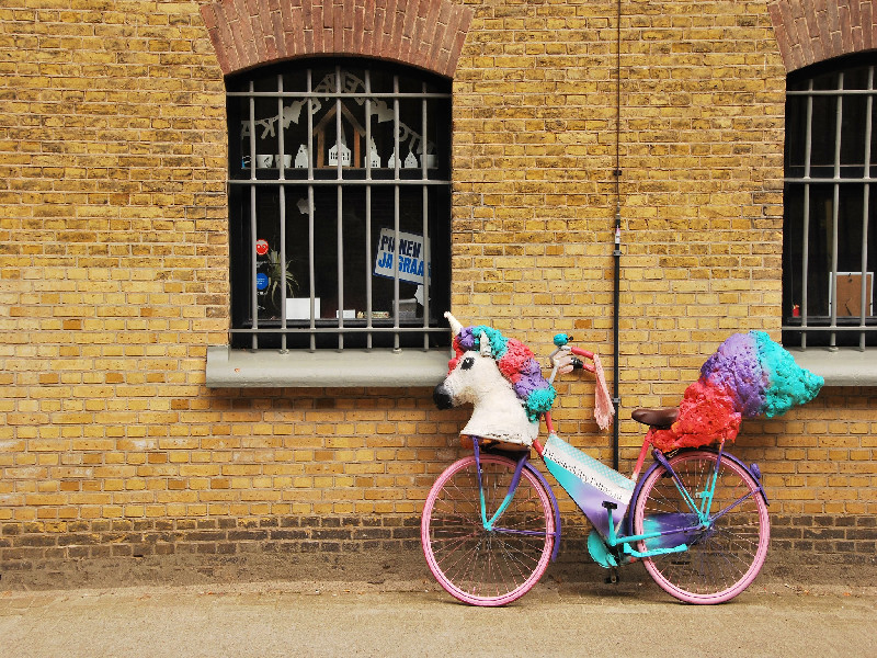 Photo of a bicycle with unicorn decoration leaning against a brick wall